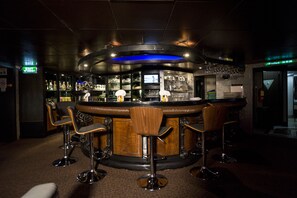 Una zona de bar con mostrador curvo, taburetes y una pantalla de televisión.