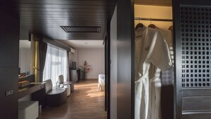 Habitación de hotel moderna con piso de madera, un área de descanso con sofá y sillones, una mesita y un armario con batas.