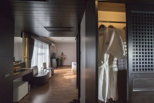 Een moderne hotelkamer met een houten vloer, een zithoek met een bank en stoelen, een kleine tafel en een garderobe met ophangjassen.