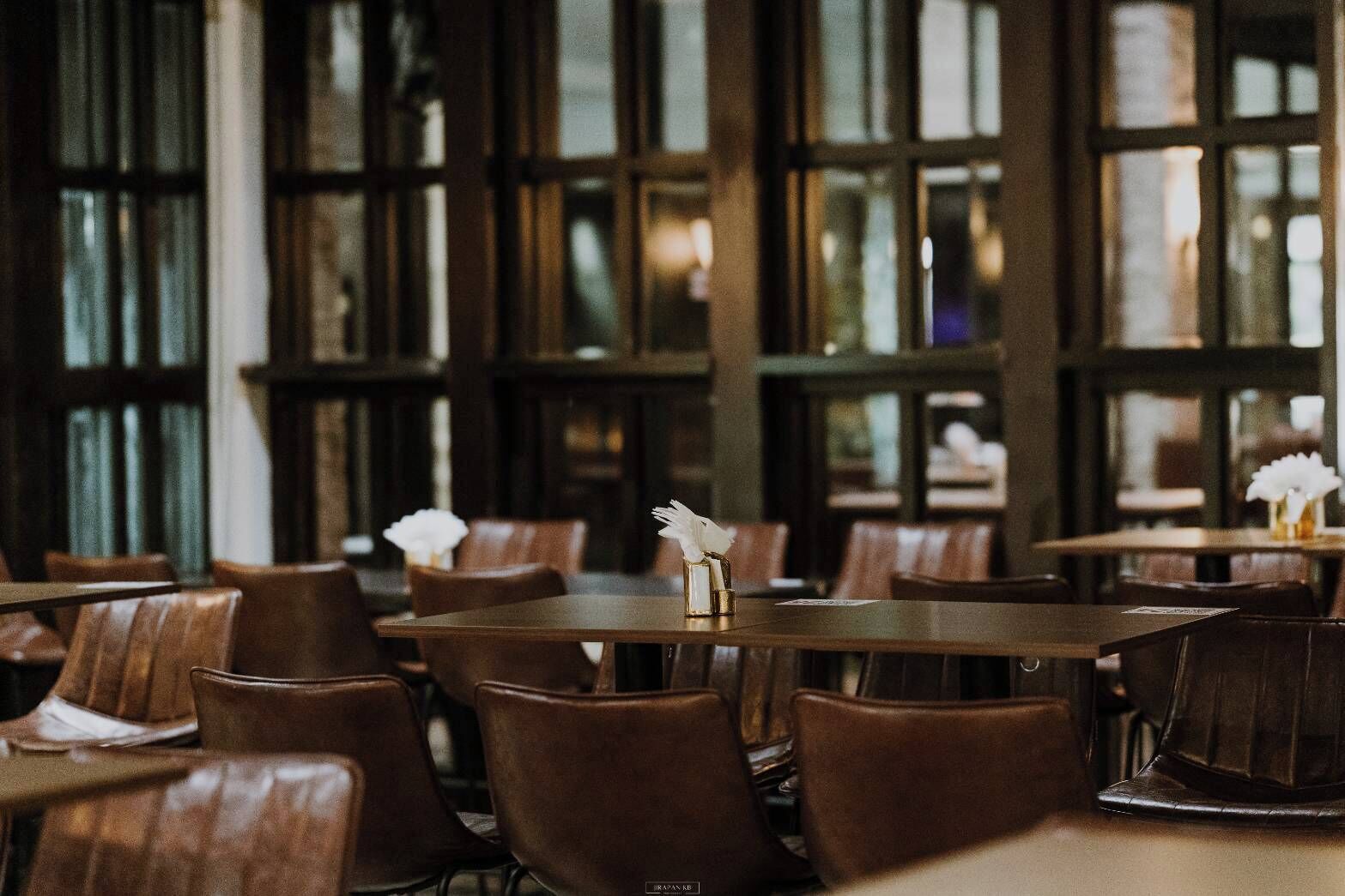 A restaurant interior with wooden tables and chairs, large windows, and a warm ambiance.