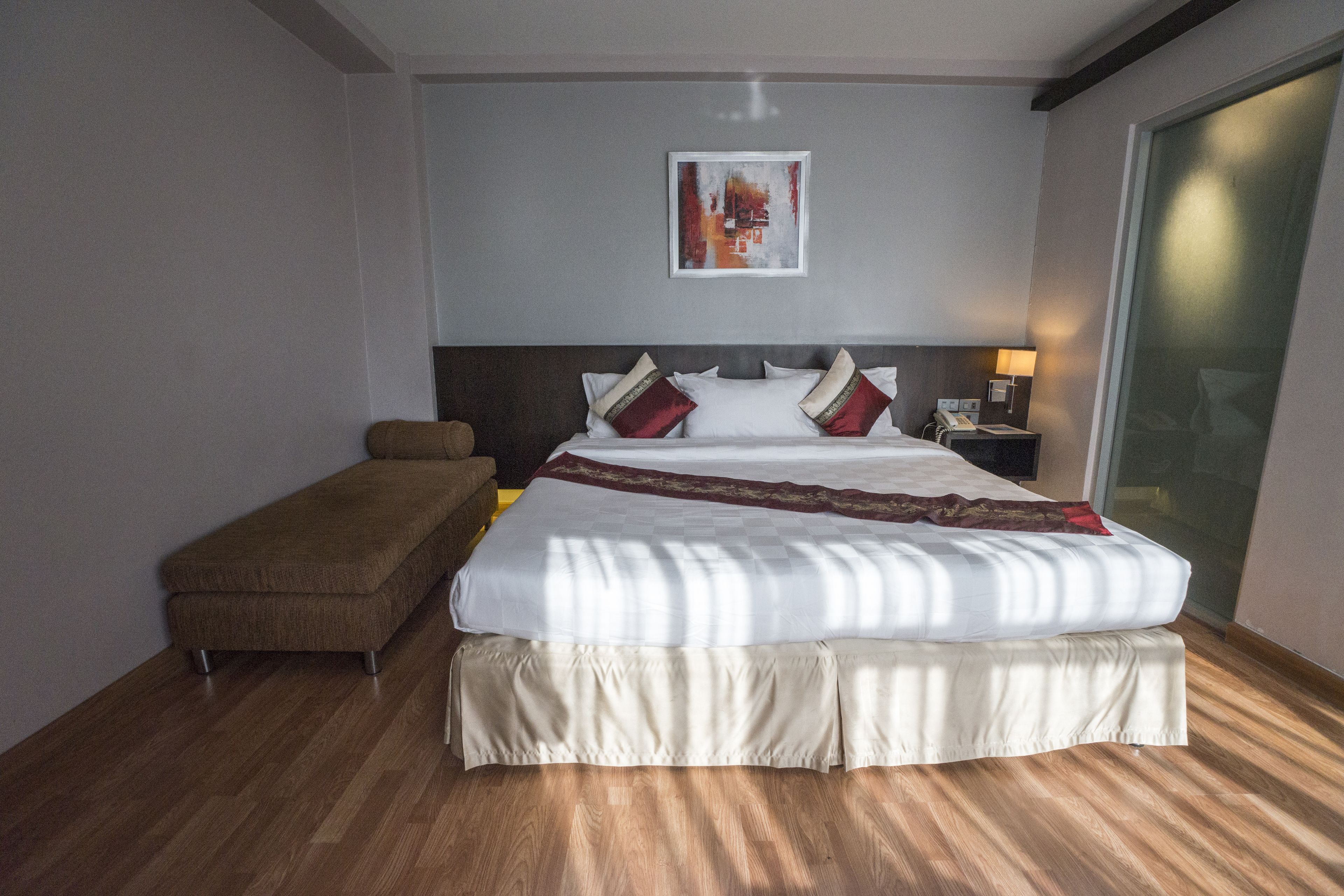 A hotel room with a large bed, a bench, a bedside table with a lamp, and a framed picture on the wall.