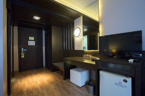 Habitación de hotel con piso de madera, un escritorio con televisor, un refrigerador pequeño y un basurero.