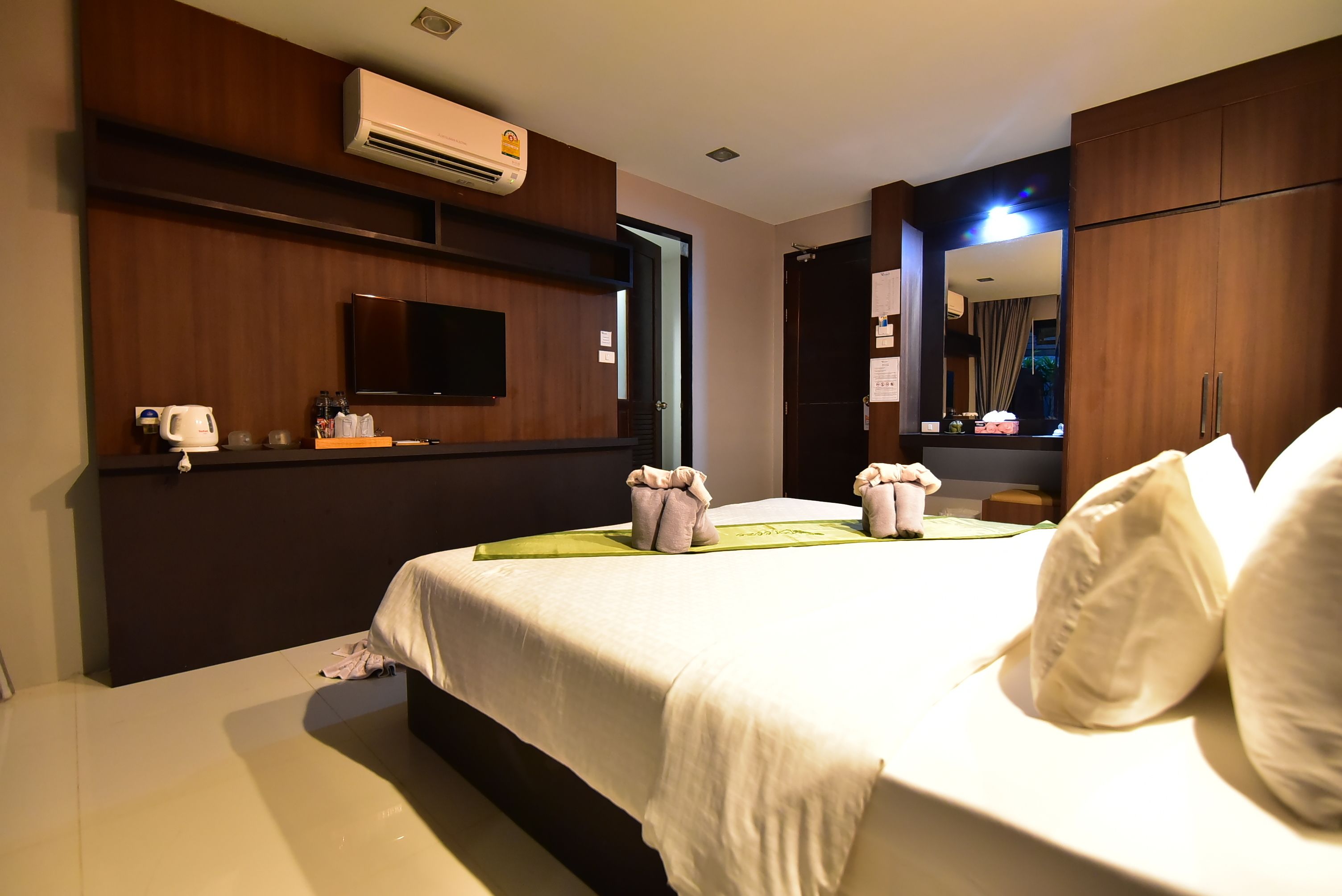 Ein Hotelzimmer mit einem großen Bett, einem flachbildfernseher an der Wand, einem Spiegel und einem Holzschrank.