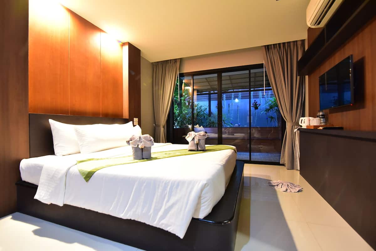 A hotel room with a large bed, a flat-screen TV, and a view of greenery outside.