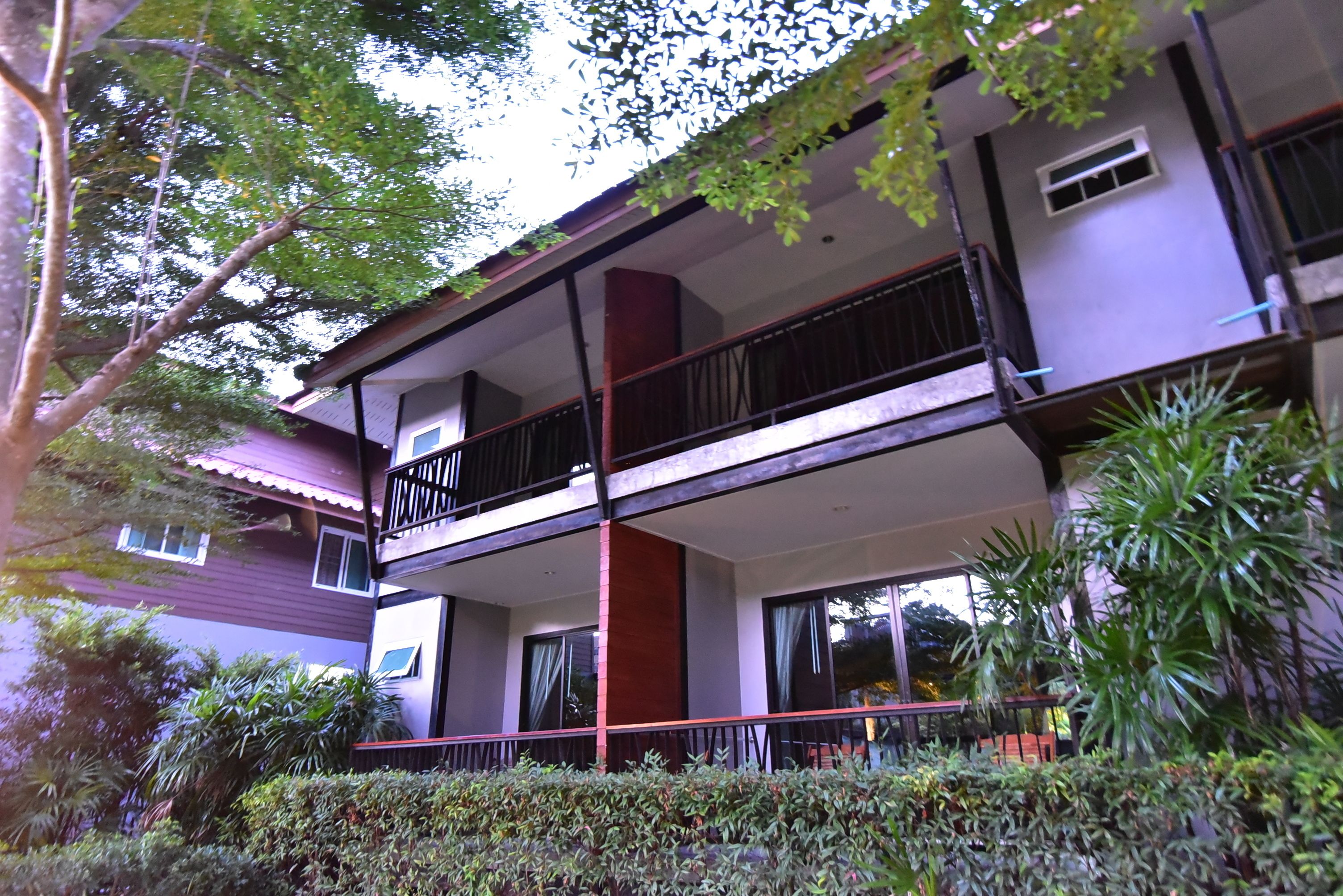 A two-story building with balconies, surrounded by greenery.
