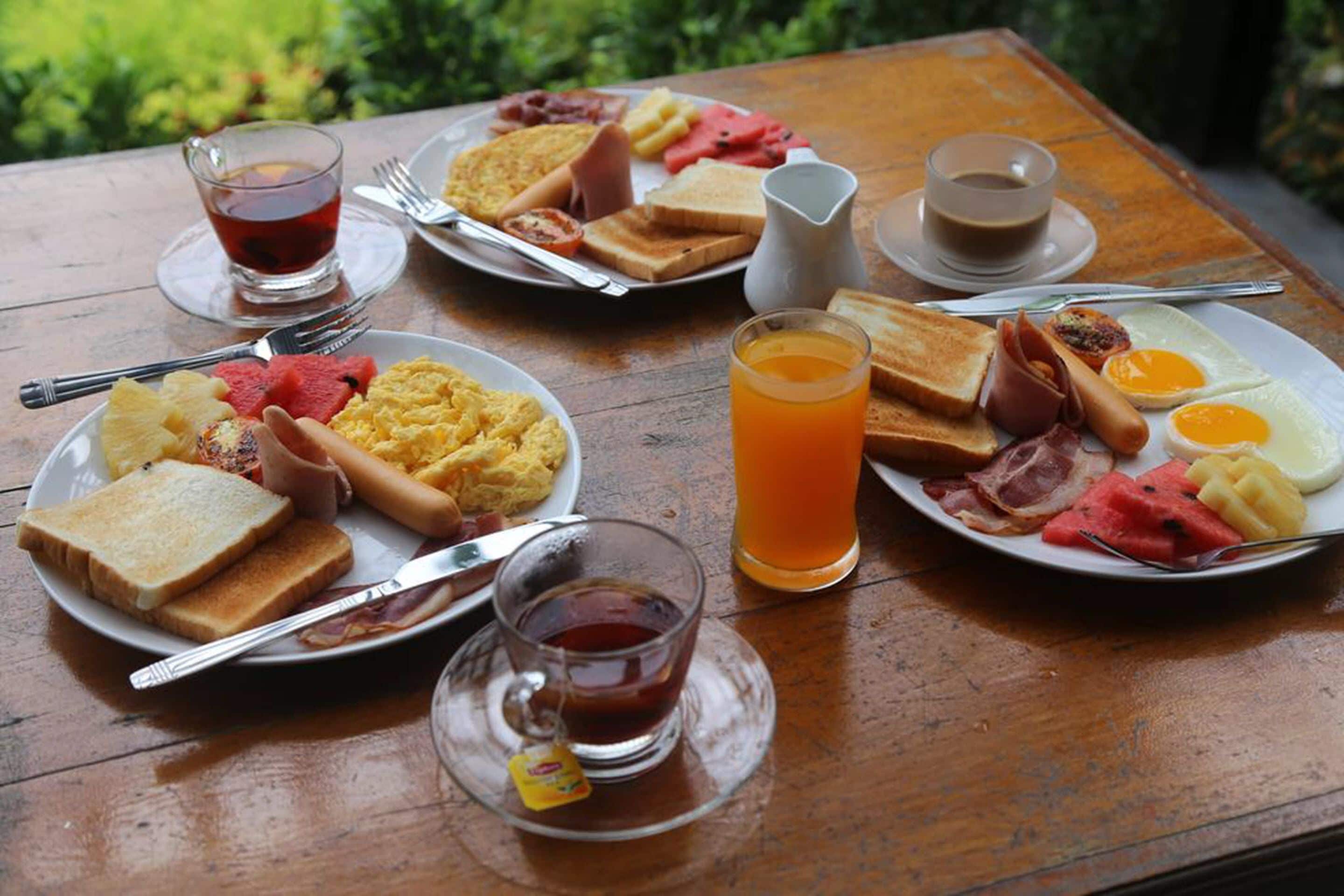 A breakfast table with plates of eggs, toast, bacon, and fruit.