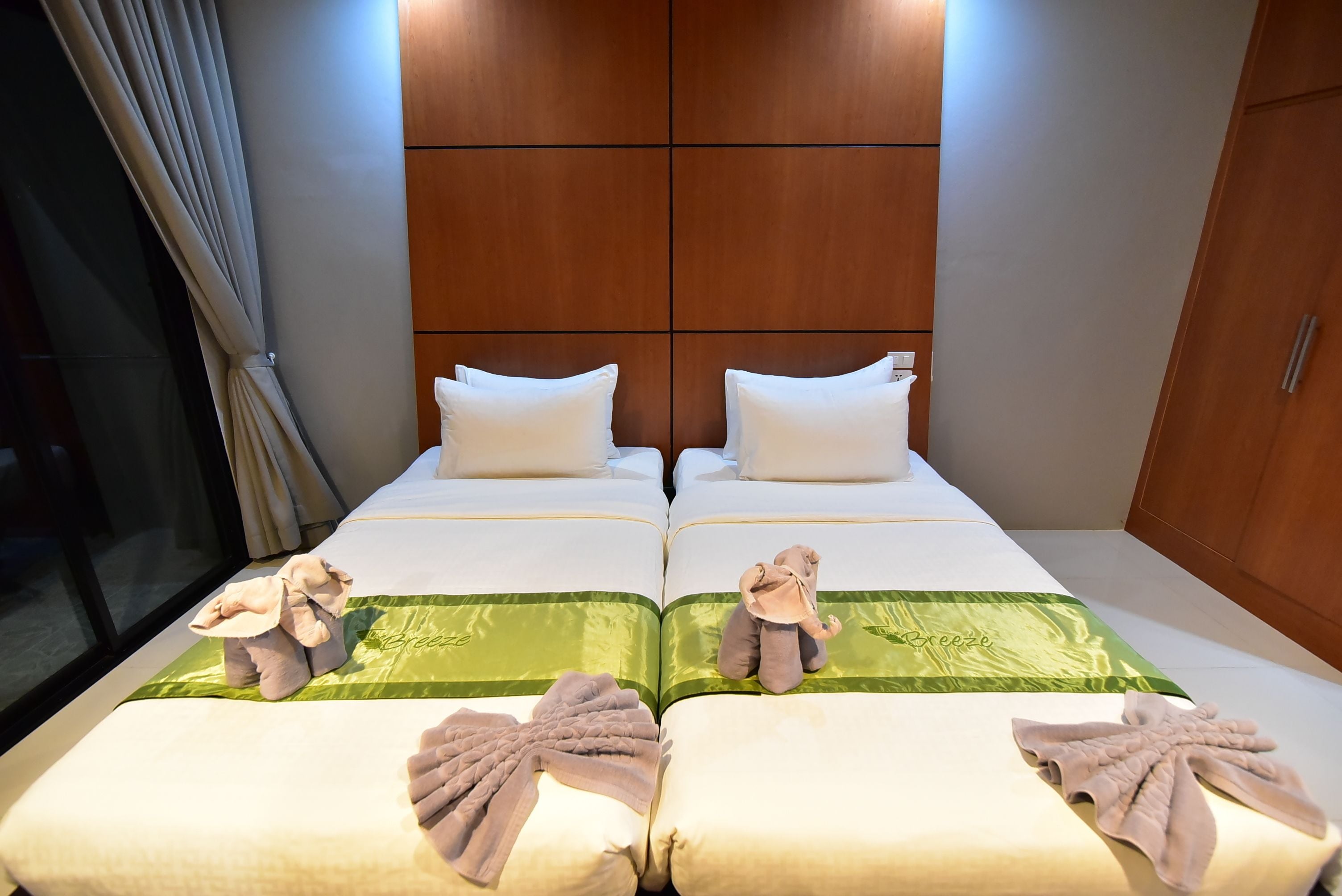 Ein Hotelzimmer mit zwei Betten, jeweils mit einer grünen Tagesdecke und einem Kuscheltier.