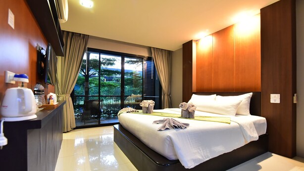 A modern hotel room with a large bed, a desk with a kettle, and a view of greenery through the window. - The Breeze Lipe Resort (Koh Lipe)