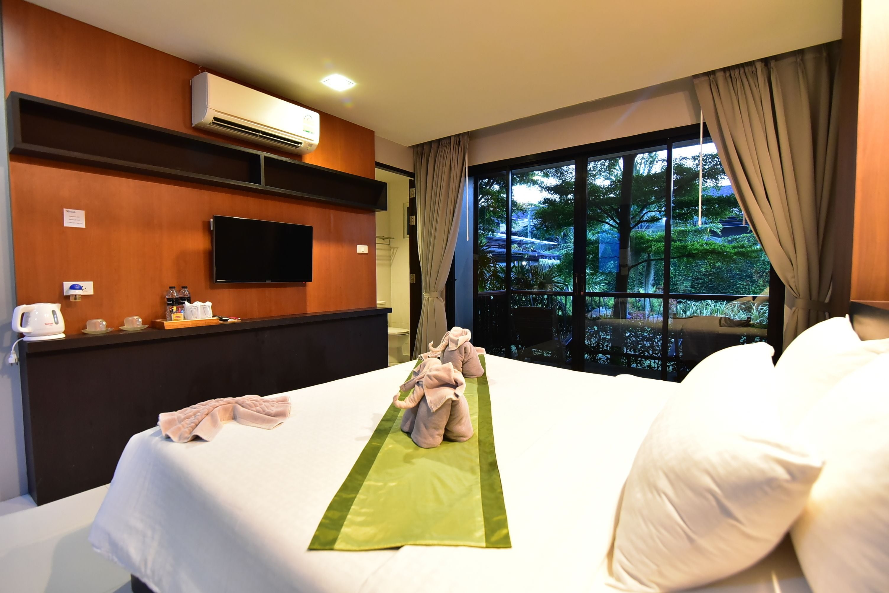 Una camera d'albergo con un letto, una TV, una finestra vista verde e un mini-frigo.