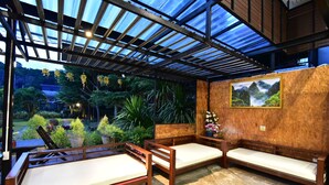 A covered outdoor seating area with wooden benches and cushions, surrounded by greenery and a view of a mountainous landscape. - The Breeze Lipe Resort (Koh Lipe)