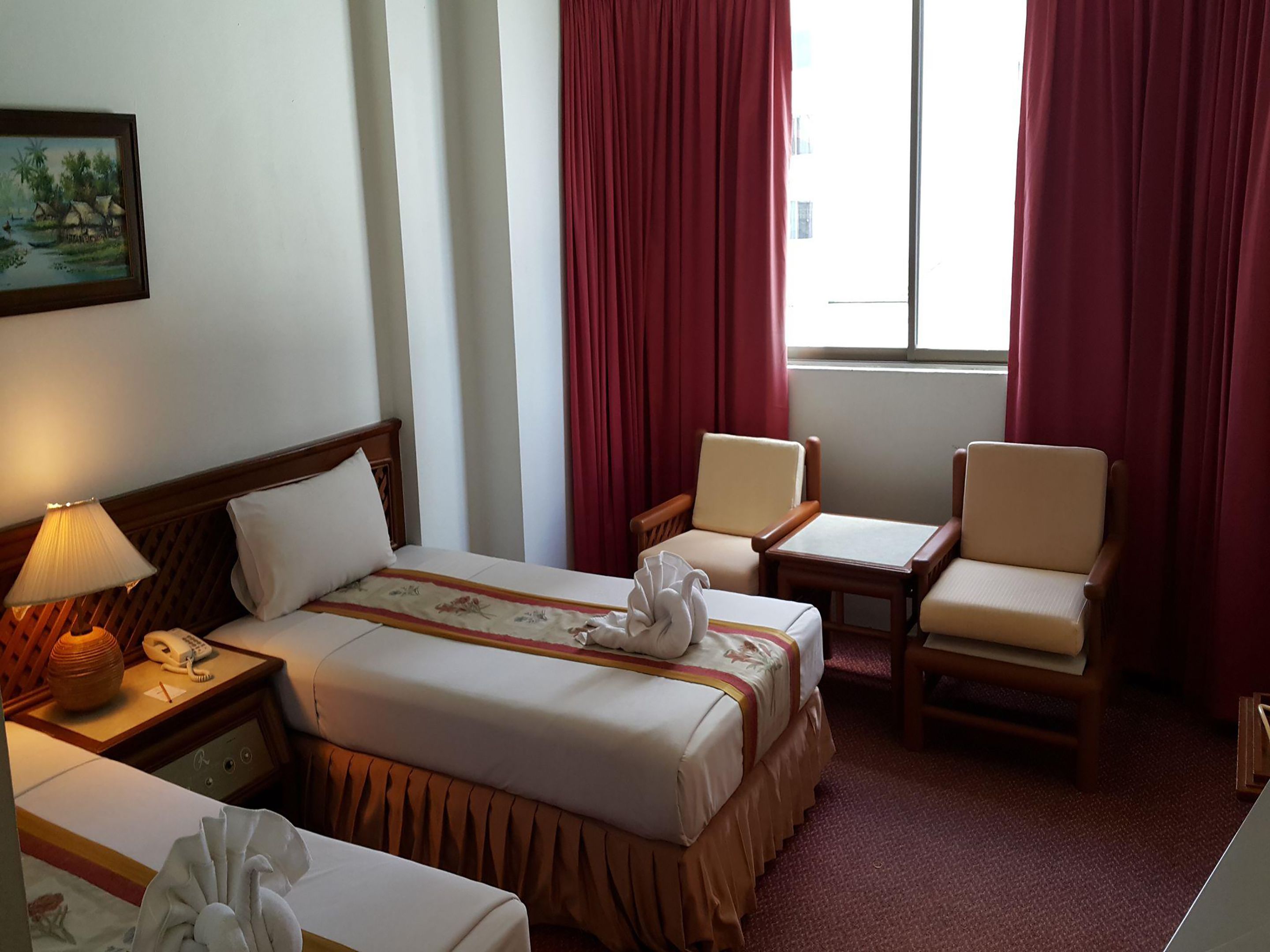 Habitación de hotel con una cama, dos sillas, una mesa, una lámpara, un teléfono y un cuadro en la pared.