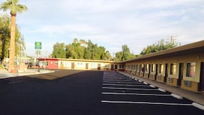 A Desert Inn motel with a row of single-story rooms, a parking lot, and a gas station in the background. - Desert Inn (Brawley)