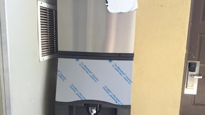A stainless steel vending machine with a water dispenser, located outside a building with a beige wall and a brown door. - Desert Inn (Brawley)