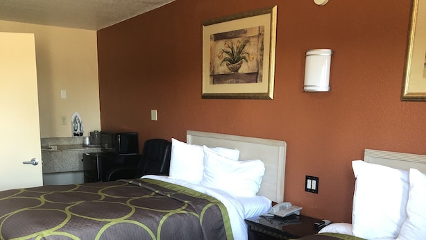 A hotel room with two beds, a desk, a chair, a small kitchenette, and a painting on the wall. - Desert Inn (Brawley)