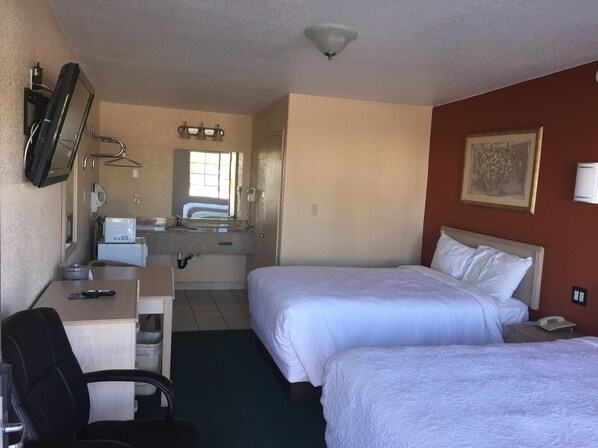 A hotel room with two beds, a desk with a chair, a desk lamp, a telephone, and a painting on the wall.