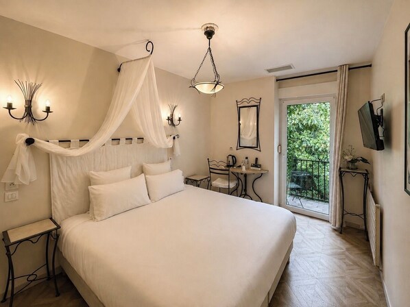 A bedroom with a bed, bedside tables, a desk, a chair, a hanging light fixture, a ceiling light, a television, and a view of greenery outside.