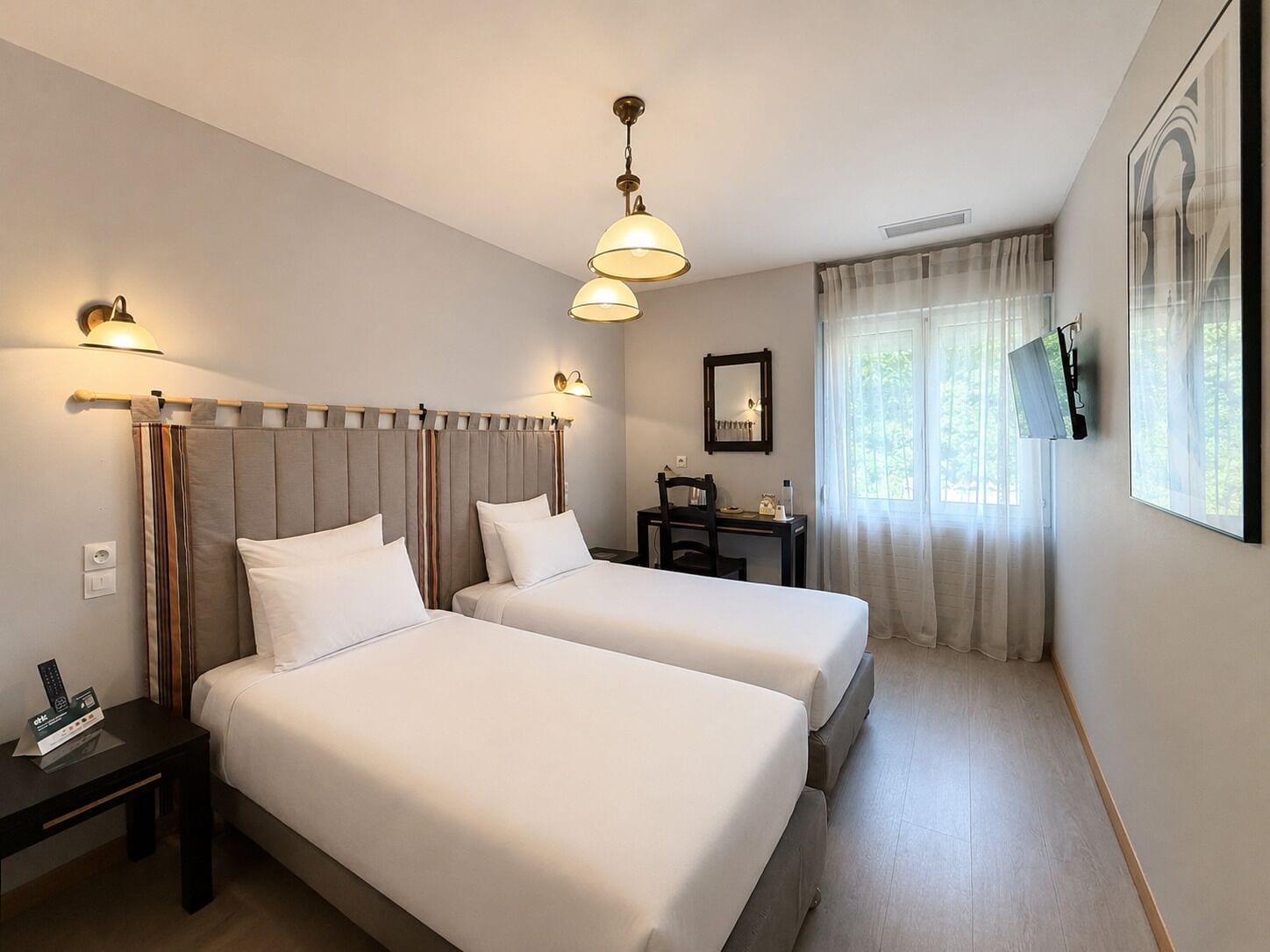 Ein Hotelzimmer mit zwei Betten, einem Schreibtisch, einem Stuhl, einem Fernseher und einem Fenster mit Vorhängen.