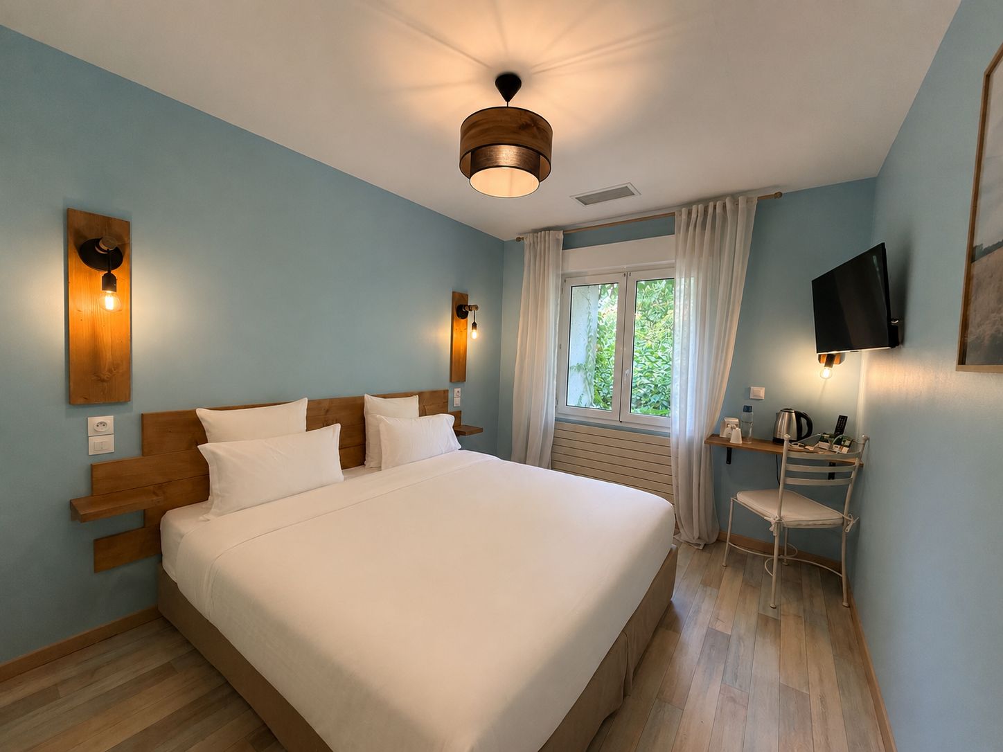 A bedroom with a bed, bedside tables, a desk with a chair, a television, and a window with curtains.