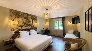 Ein Hotelzimmer mit einem großen Bett, einem Schreibtisch, zwei Stühlen, einem Fernseher und einer Wandmalerei mit einem Baum.