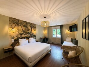 A hotel room with a large bed, a desk, two chairs, a television, and a tree mural on the wall.