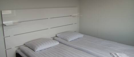 Una cama con dos plazas, cabecera blanca y dos almohadas.
