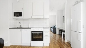 Una cocina moderna con armarios blancos, microondas integrado, lavavajillas y estufa. Se ve un comedor con una mesa y sillas al fondo.