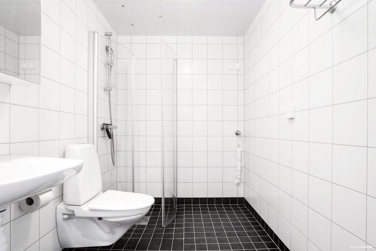 Un bany modern amb rajoles blanques, un vàter, un lavabo i una dutxa amb envàs de vidre.