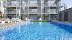 Un hotel moderno con piscina, varios balcones y sillones de descanso.