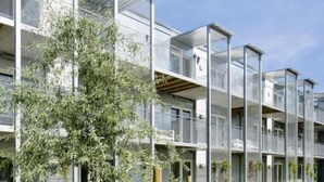 Un edificio moderno con varios balcones, un patio césped y un árbol.