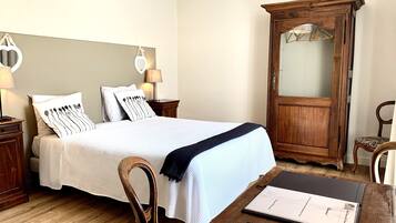 Une chambre d’hôtel bien aménagée, avec un lit, des tables de chevet, une armoire en bois, une chaise et un bureau équipé d’une télécommande et d’un carnet.