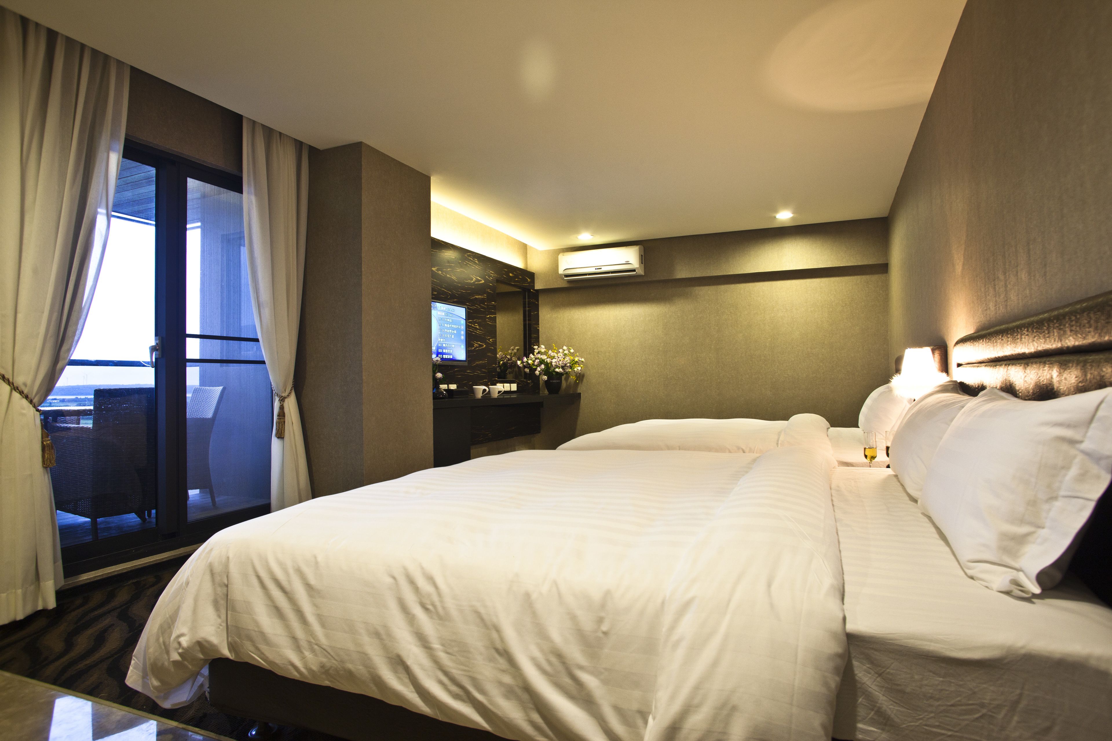 A hotel room with a large bed, a desk with a computer, and a view of the outdoors through a sliding door.