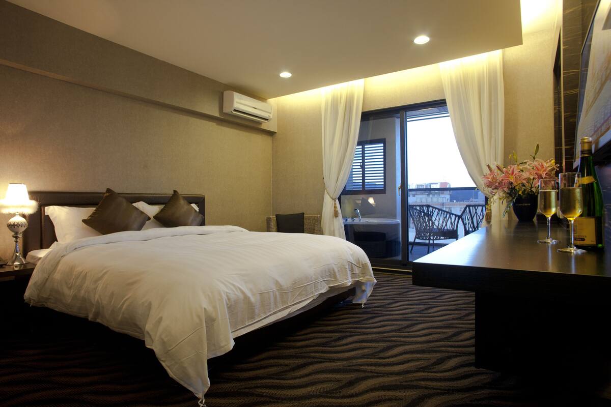 Habitación de hotel con una cama grande, un escritorio con un florero y vistas a la ciudad desde la ventana.