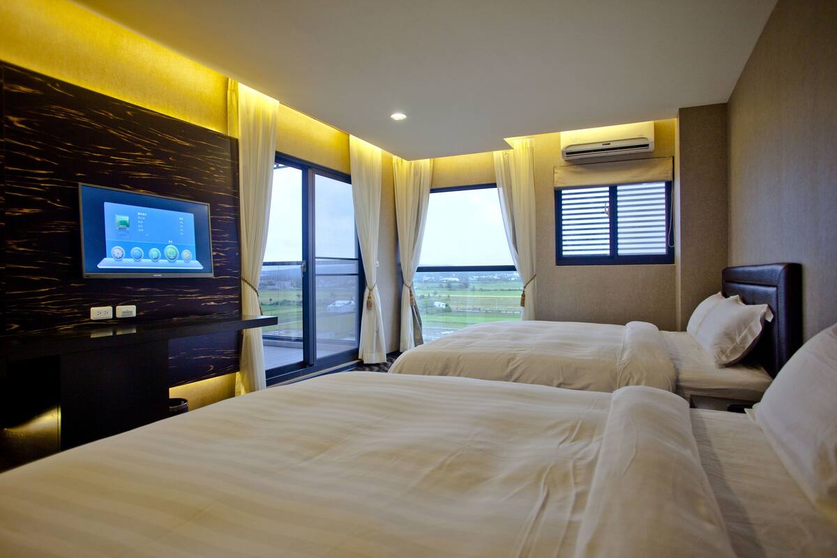 Habitación de hotel con dos camas, un televisor y un ventanal con vistas.