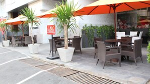 An outdoor seating area with wicker chairs and orange umbrellas, a palm tree planter, and a sign for the Thusuputamu Hotel. - Sotis Hotel Falatehan Jakarta (Jakarta)