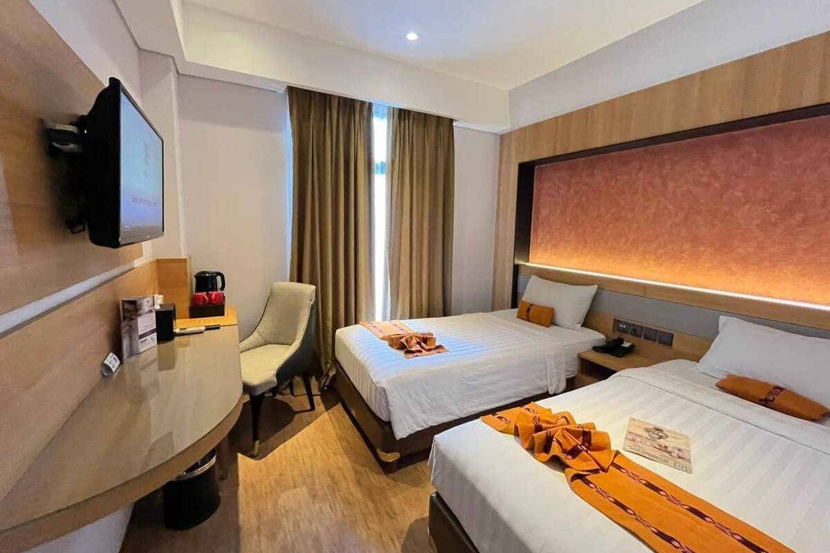 Una habitación de hotel con dos camas, un escritorio, una silla, un televisor y una ventana con cortinas.