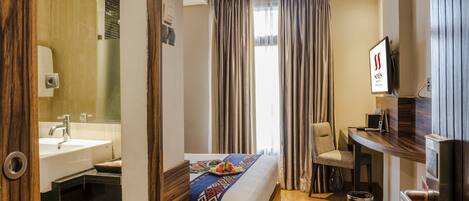 A hotel room with a bed, a desk, a chair, a sink, and a mirror.