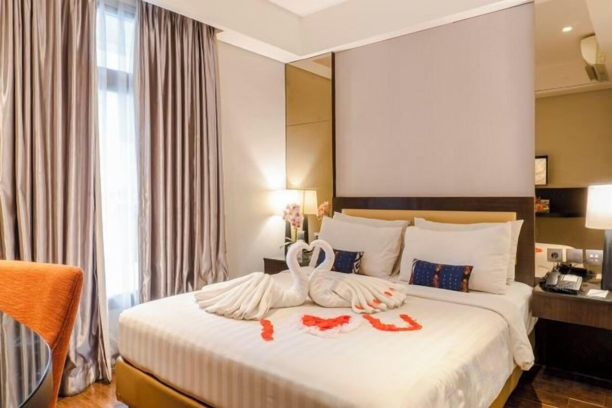 A hotel room with a large bed, a nightstand, a chair, and a mirror.