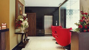 A modern lobby with a reception desk, red chairs, a wooden panel wall, and a large vase of flowers. - Sotis Hotel Falatehan Jakarta (Jakarta)