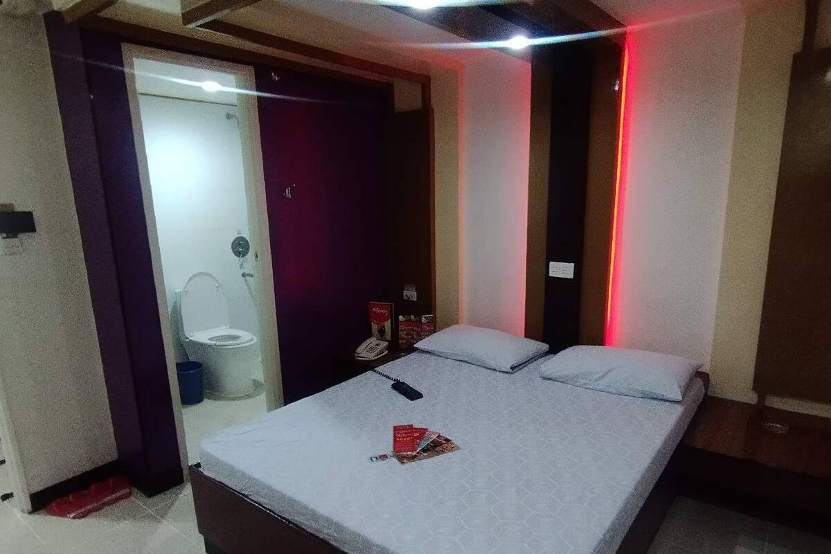 A bedroom with a bed, a small table, a chair, and a bathroom visible through an open door.