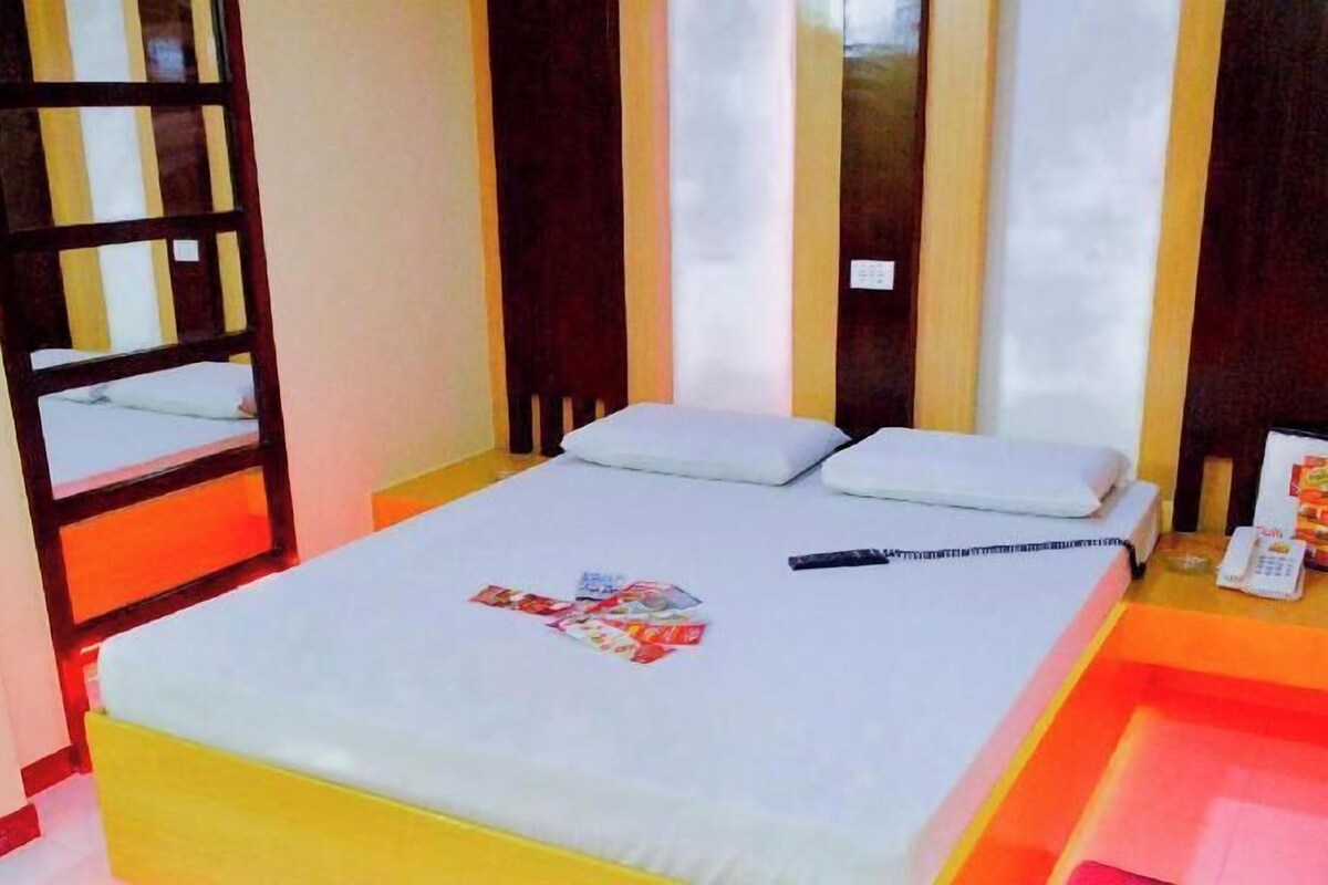 A hotel room with a bed, a bedside table with a phone, and a window with curtains.