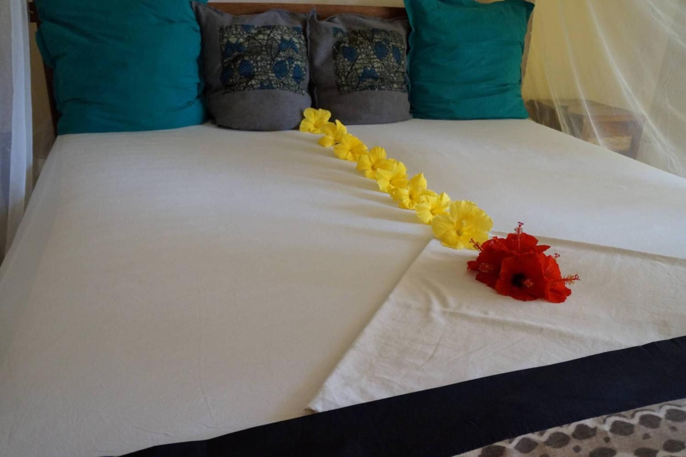 Ein Bett mit weißer Bettdecke, einem gelben Blumenkranz und einer roten Blume.