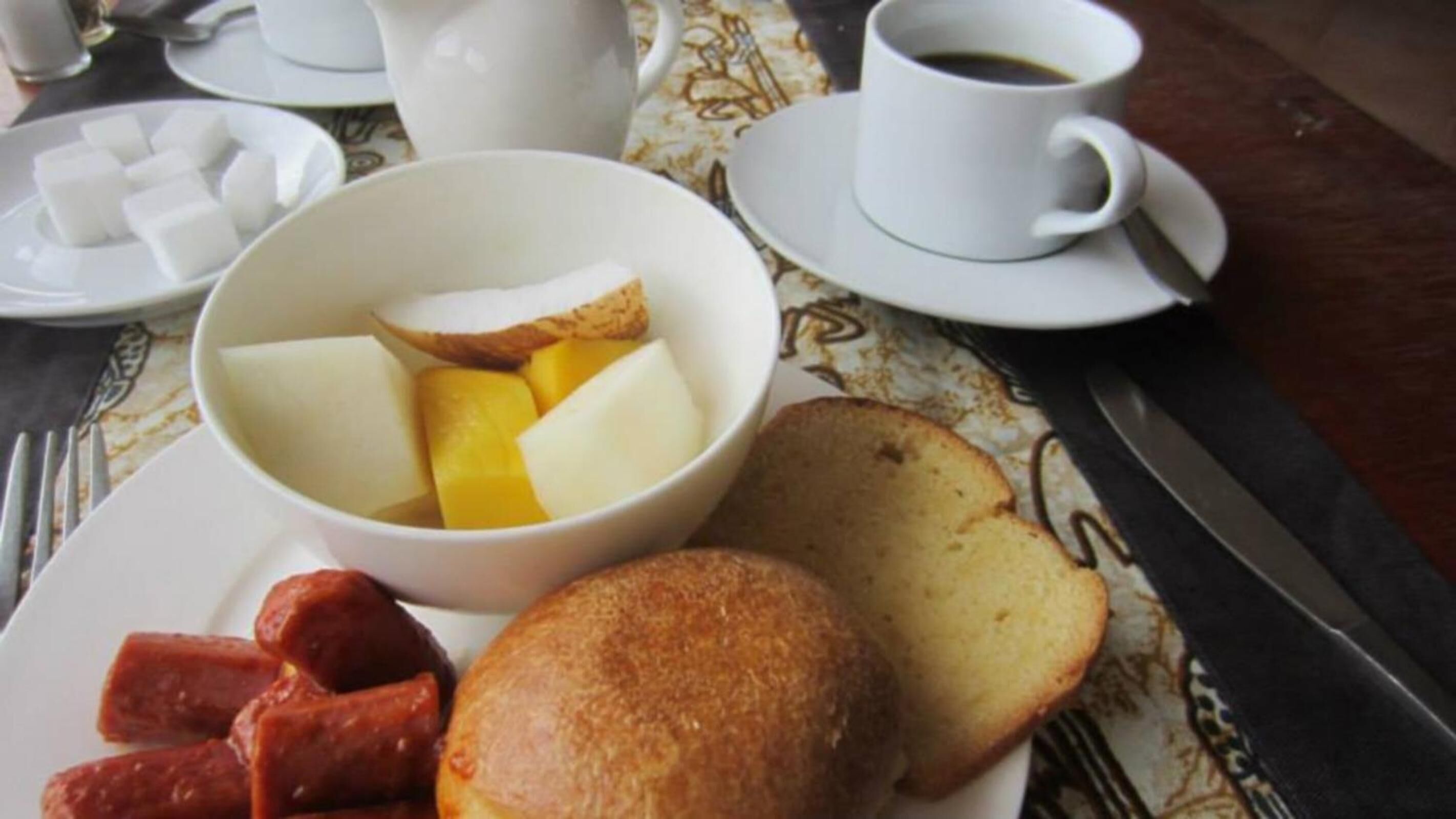 A breakfast setting with a plate of toast, sausage, and a bowl of fruit and butter.
