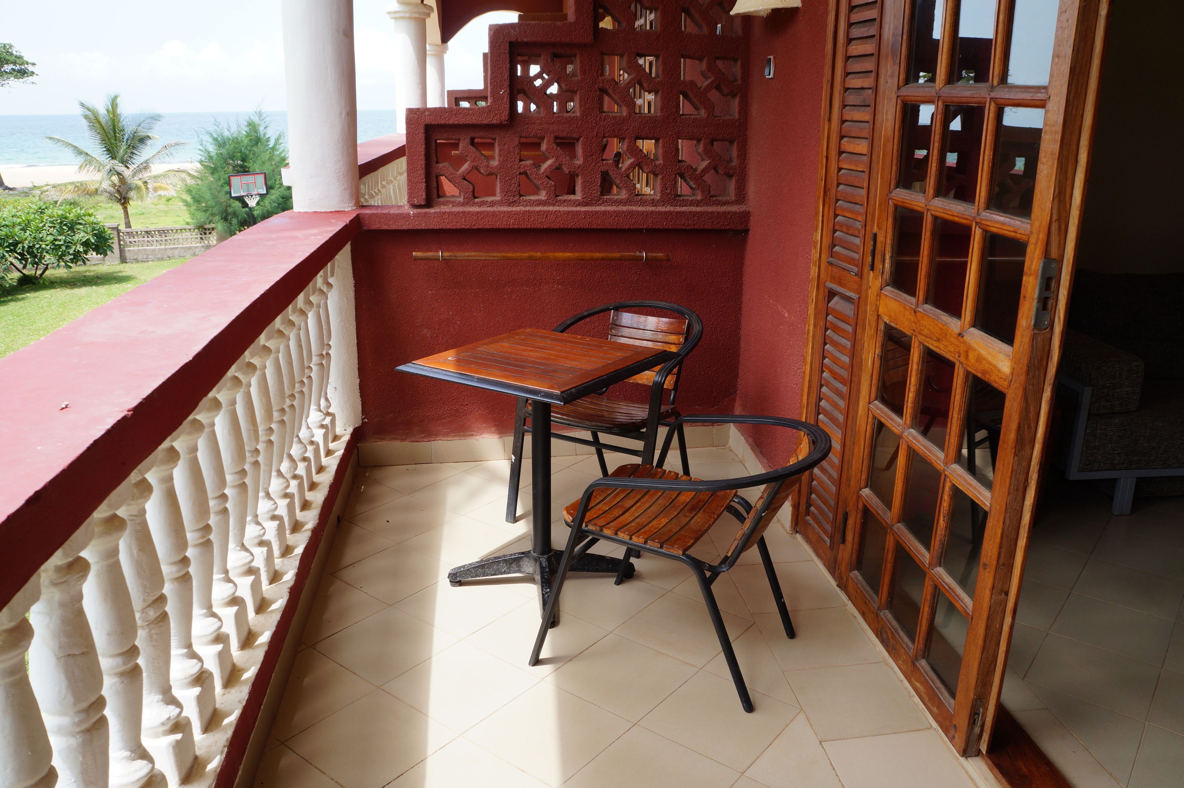 Un balcón con una mesa y dos sillas, una puerta de madera y vista a la playa.