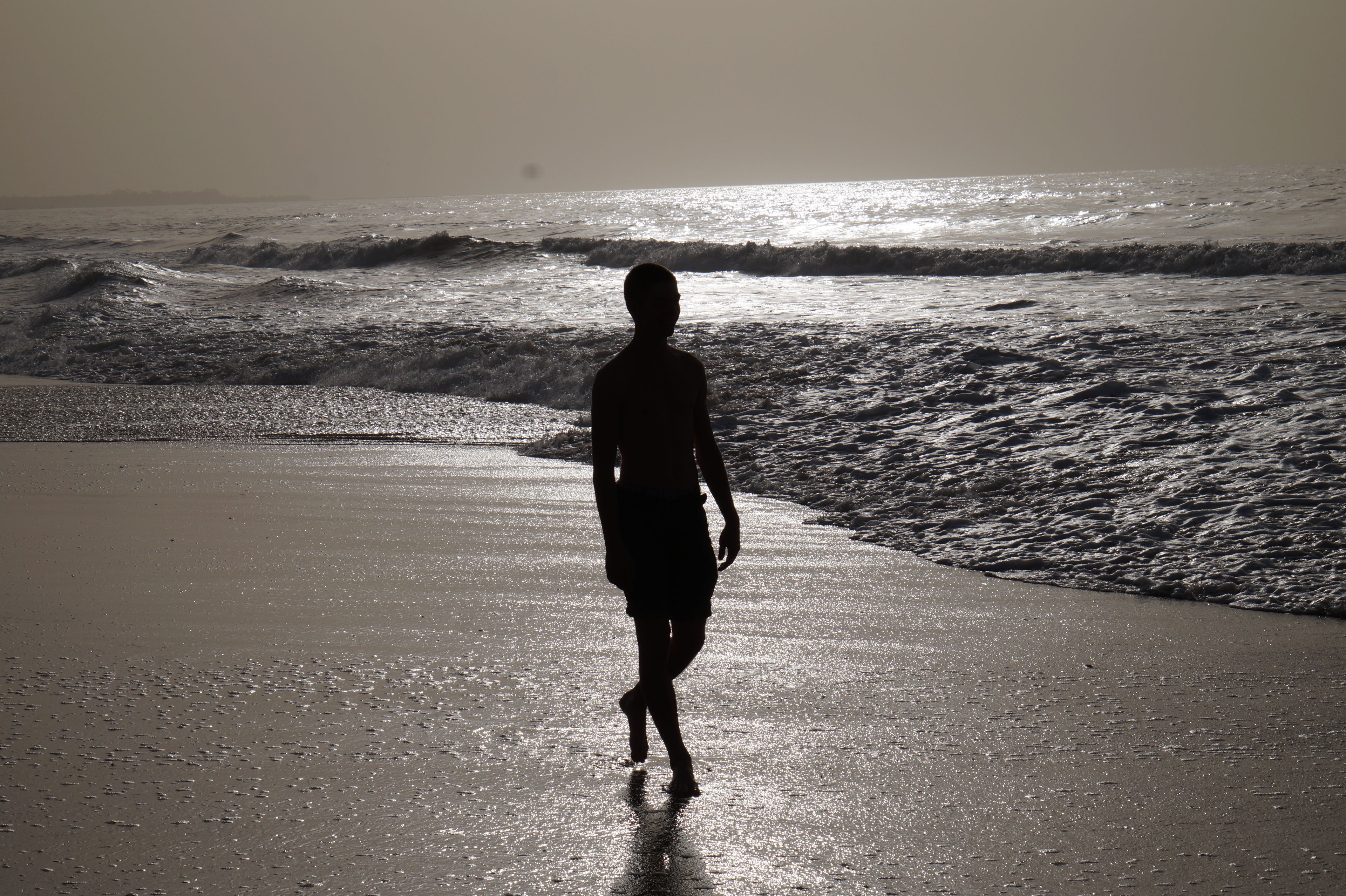 A silhouette of a person walking on a beach with waves in the background.