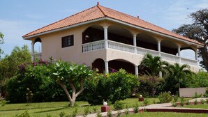 Ein zweistöckiges Gebäude mit rotem Ziegeldach, mehreren Balkonen und einem Garten mit verschiedenen Pflanzen und Blumen.
