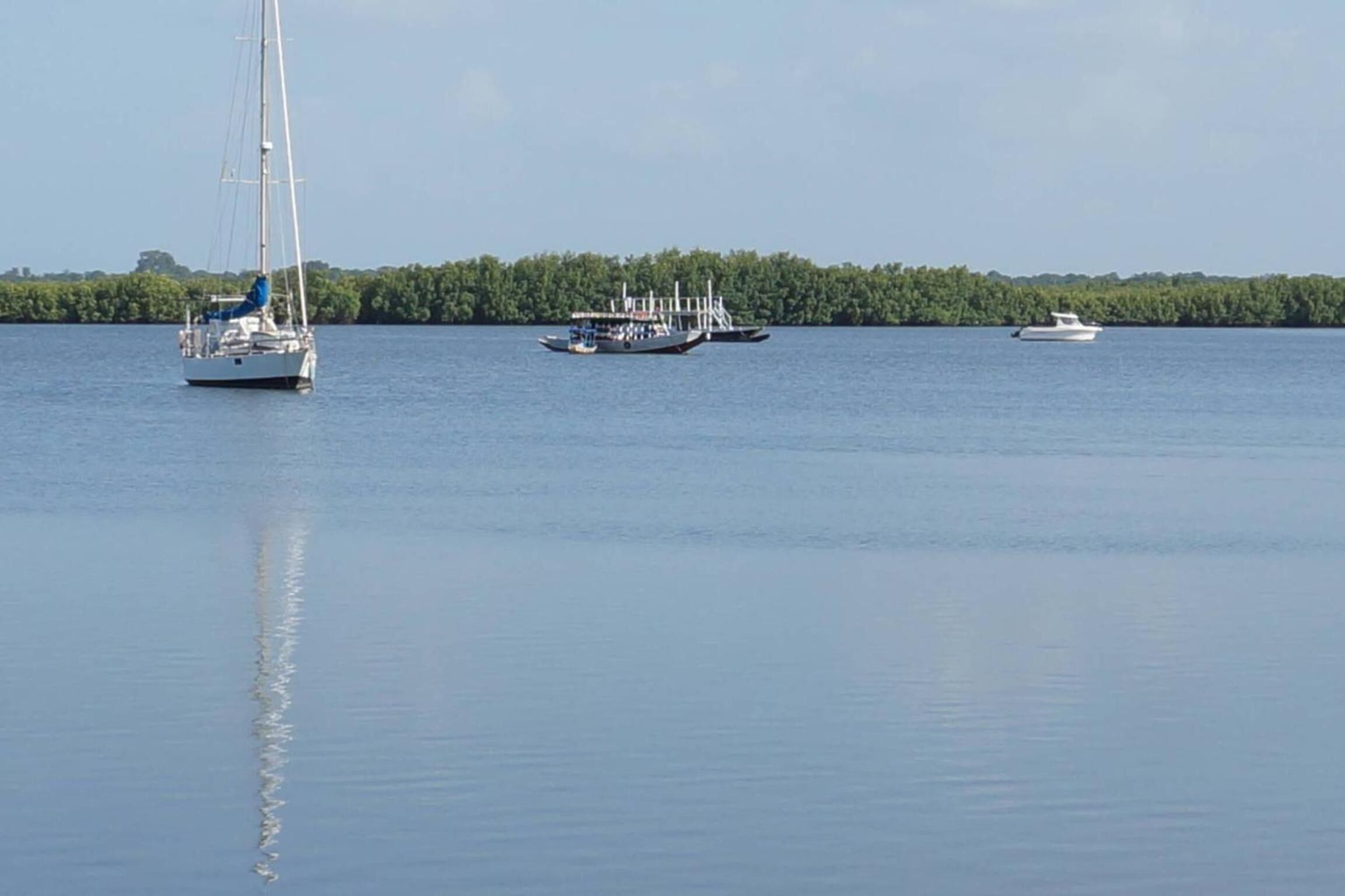 A calm lake with three boats: a sailboat, a motorboat, and a small white boat.