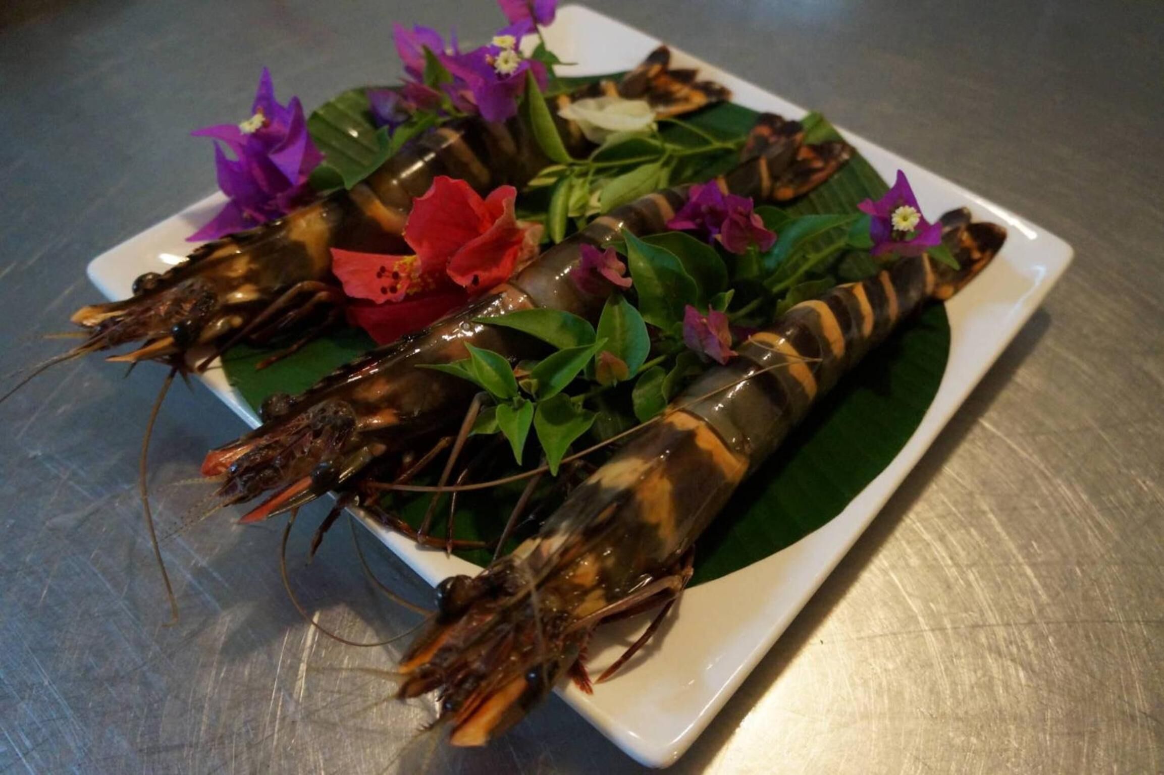 Un plato de camarones cocidos decorado con flores y hojas verdes.