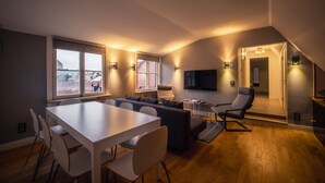 Een moderne woonkamer met een eethoek, een aan de muur bevestigde televisie en een uitzicht op de skyline door grote ramen.