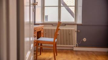 Una habitación con un escritorio y silla de madera, un radiador y una ventana con vista a un edificio.