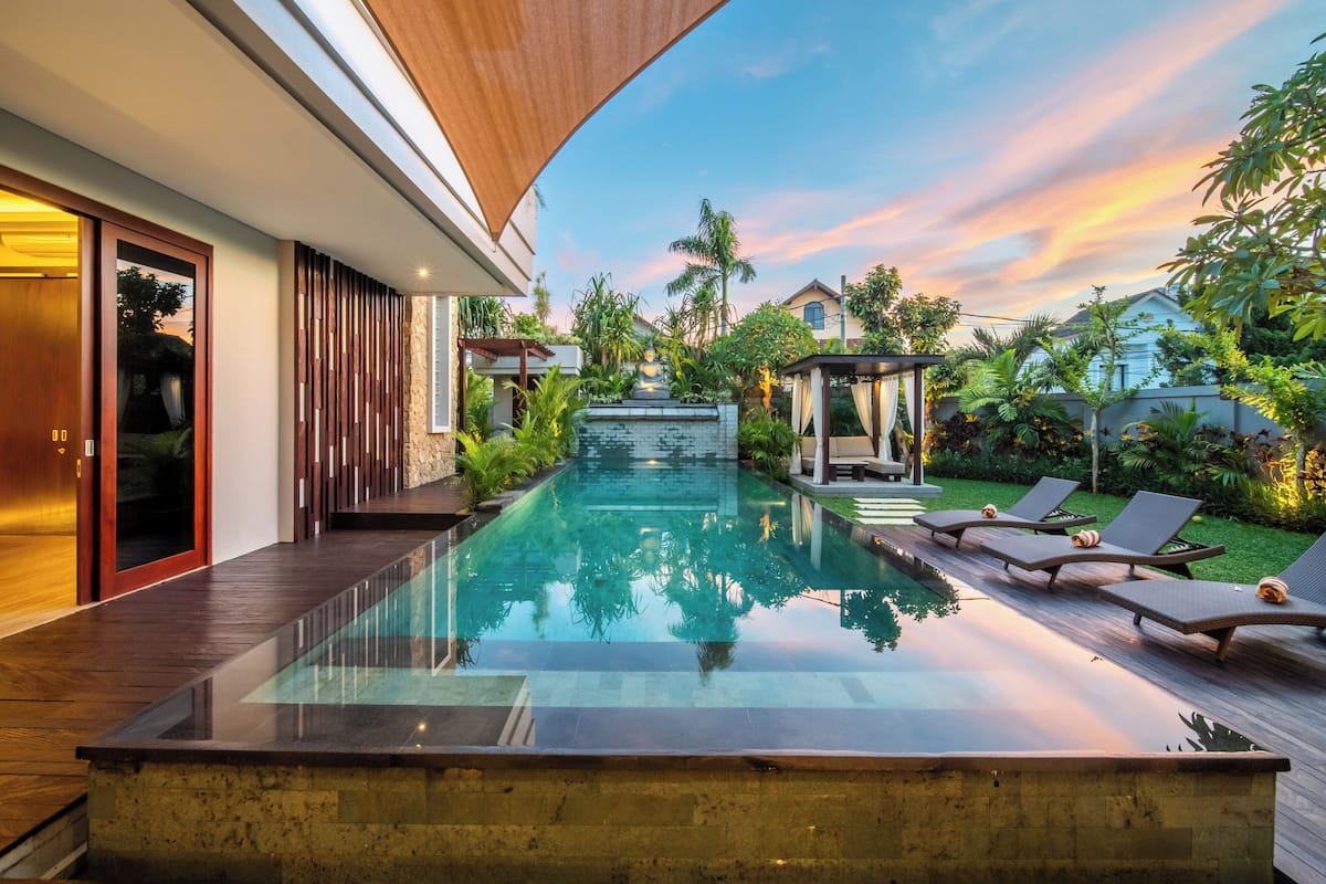 A modern outdoor pool area with a glass barrier, wooden deck, and lounge chairs.